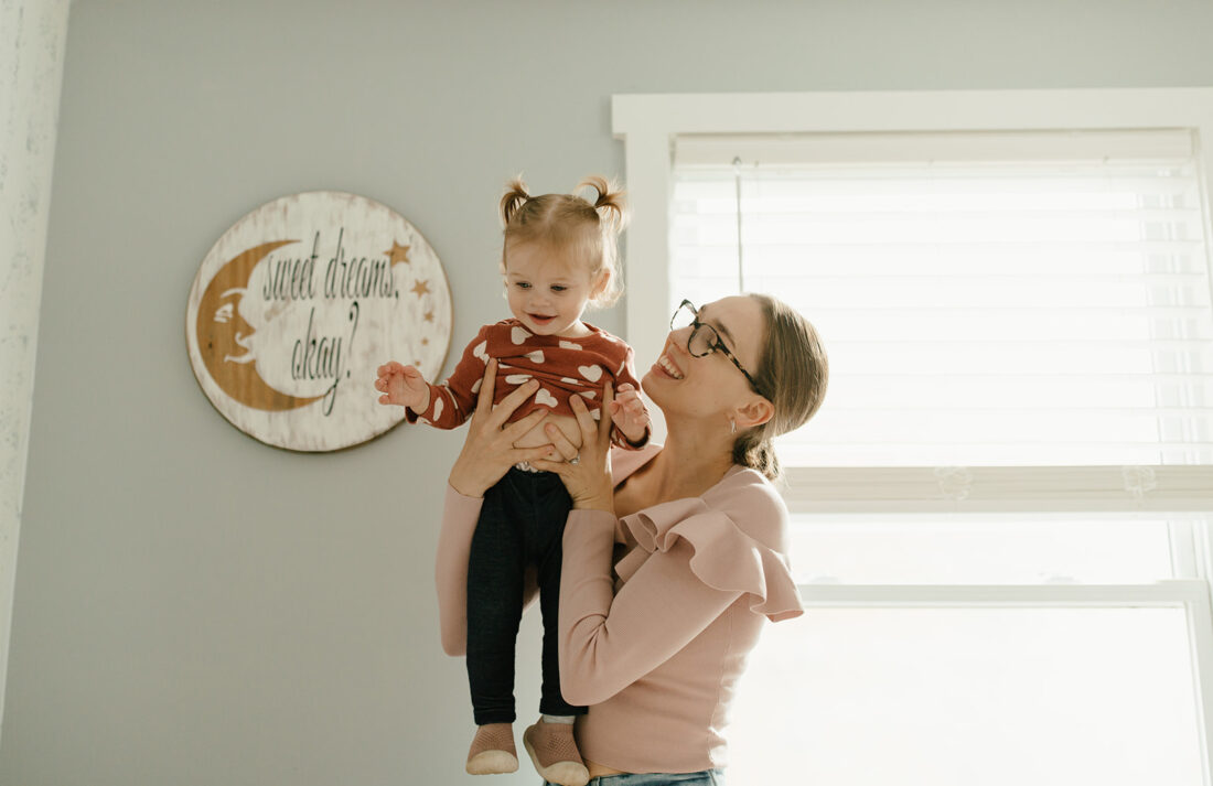 Mom and toddler smiling as mom lifts toddler above her head