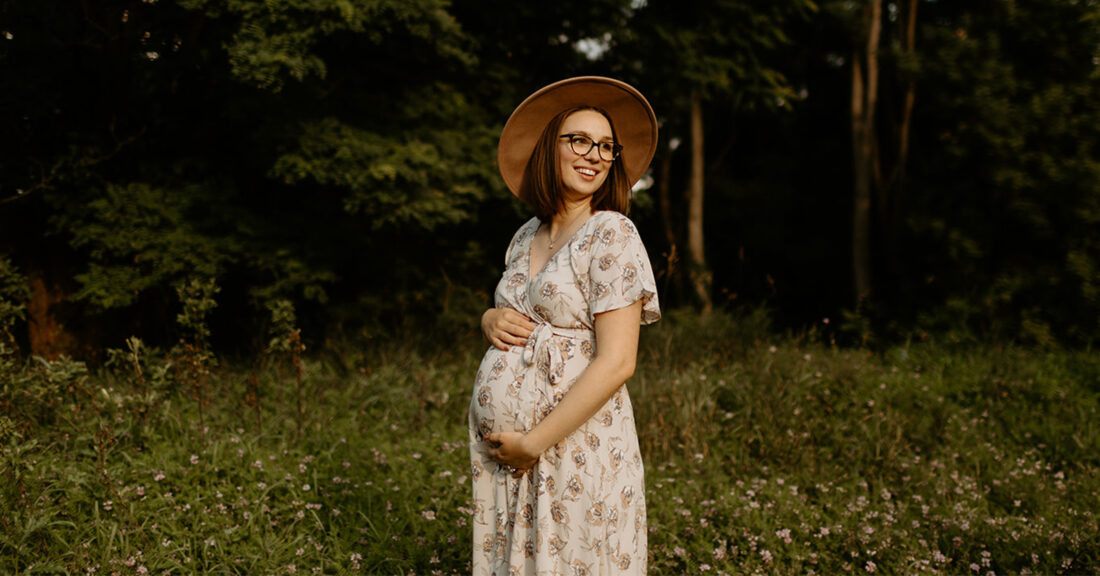 Pregnant Emaly stands in a field holding her stomach